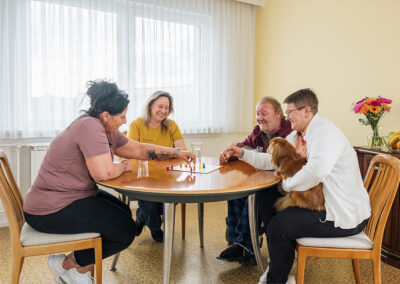 Drei Pflegekräfte und ein Bewohner beim Brettspiel in einer gemütlichen Runde