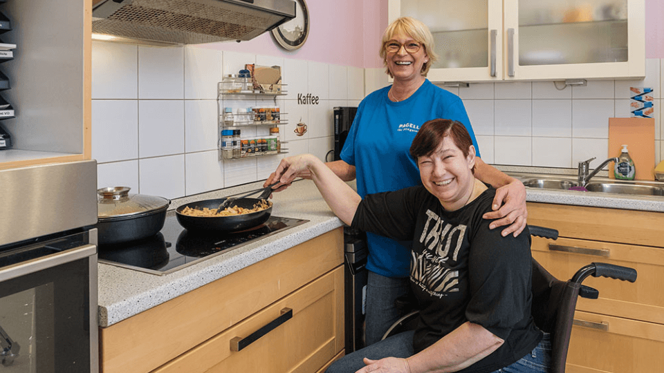 Pflegekraft unterstützt eine Frau im Rollstuhl beim Kochen